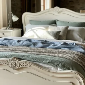 Close-up of a charming French country style bed with a distressed white finish and carved wood details, the focal point of a rustic bedroom.