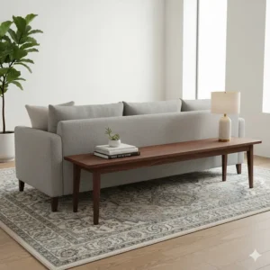 Decorative long wood bench placed behind a sofa, acting as a console table for books and lamps.