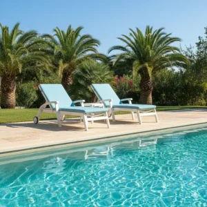 Pair of classic white resin chaise lounge chairs resting by the edge of a swimming pool.