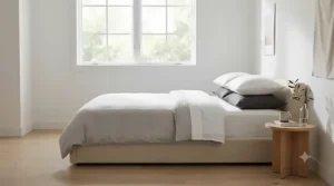 Low-profile beige upholstered bed frame placed beneath a window in a headboard-free bedroom.